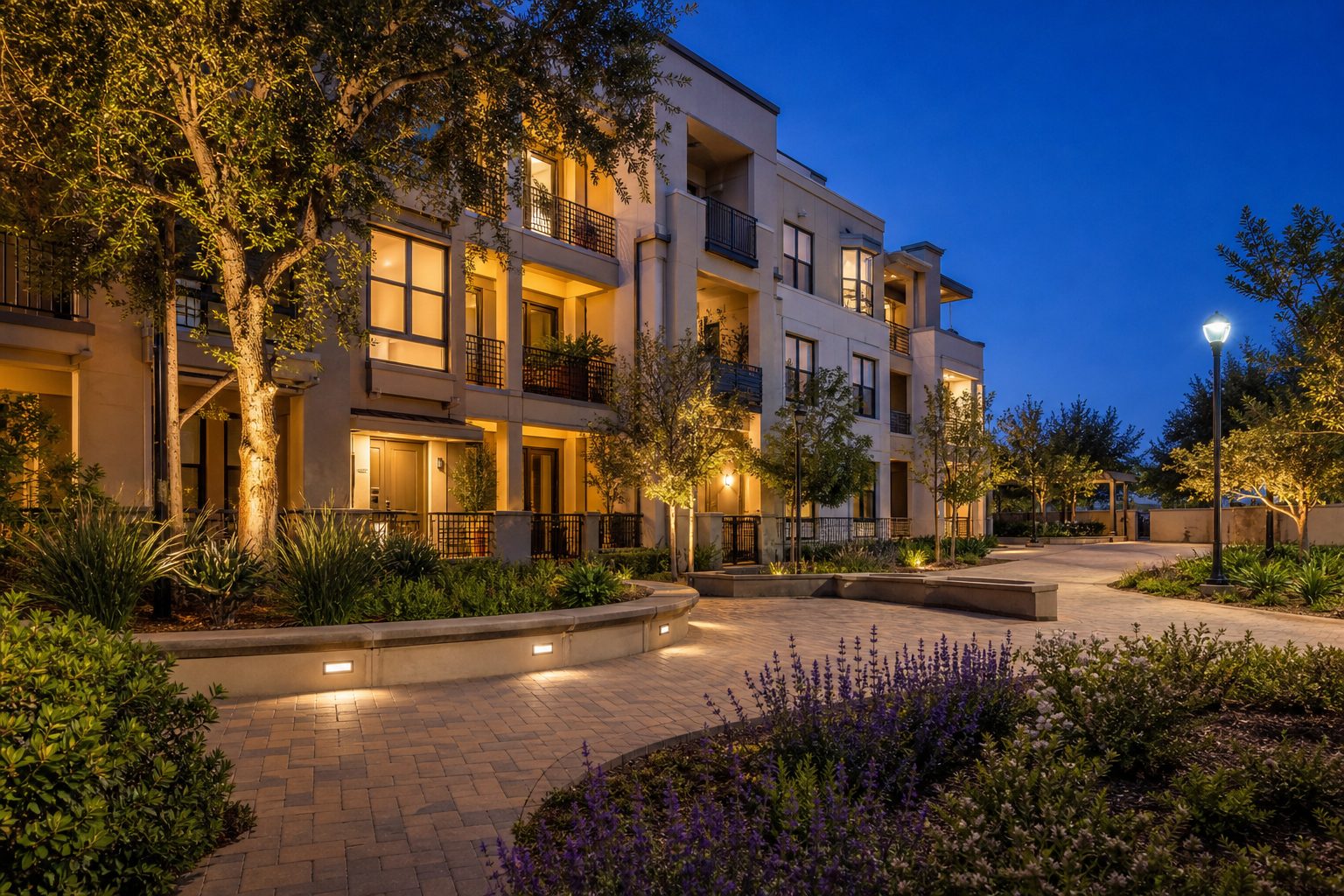 Well-maintained mid-rise condo building with warm interior lighting and professional landscaping in Alta Vista Valencia during twilight.