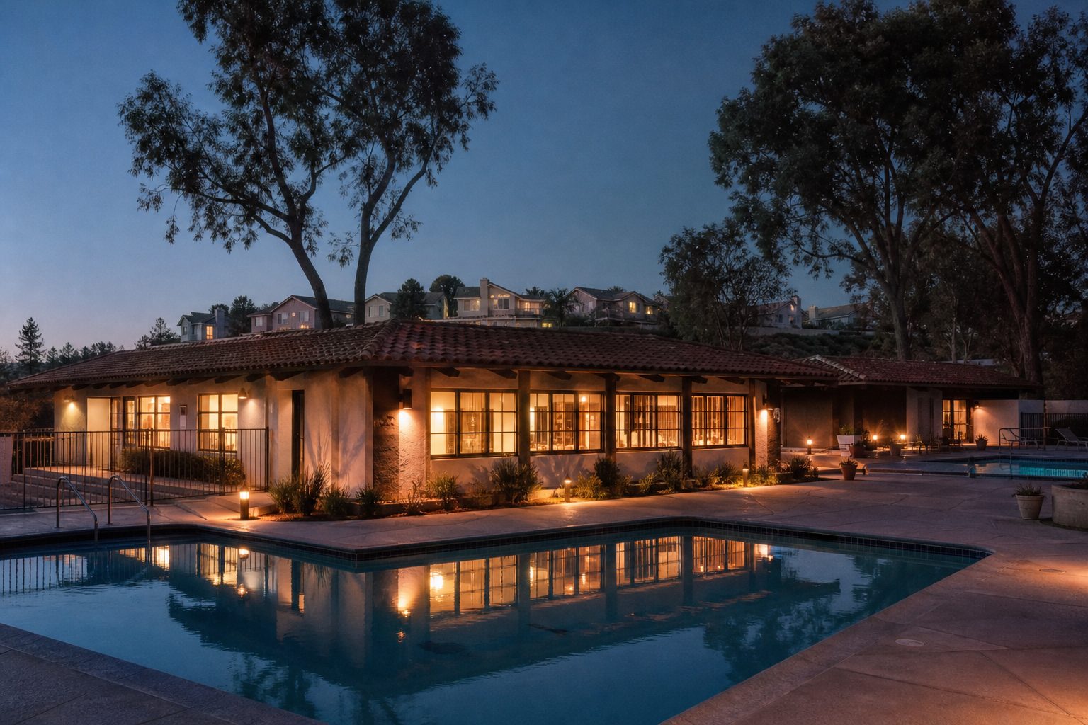 Community clubhouse and pool at Old Orchard 2 in Santa Clarita illuminated during twilight with residential homes in background.