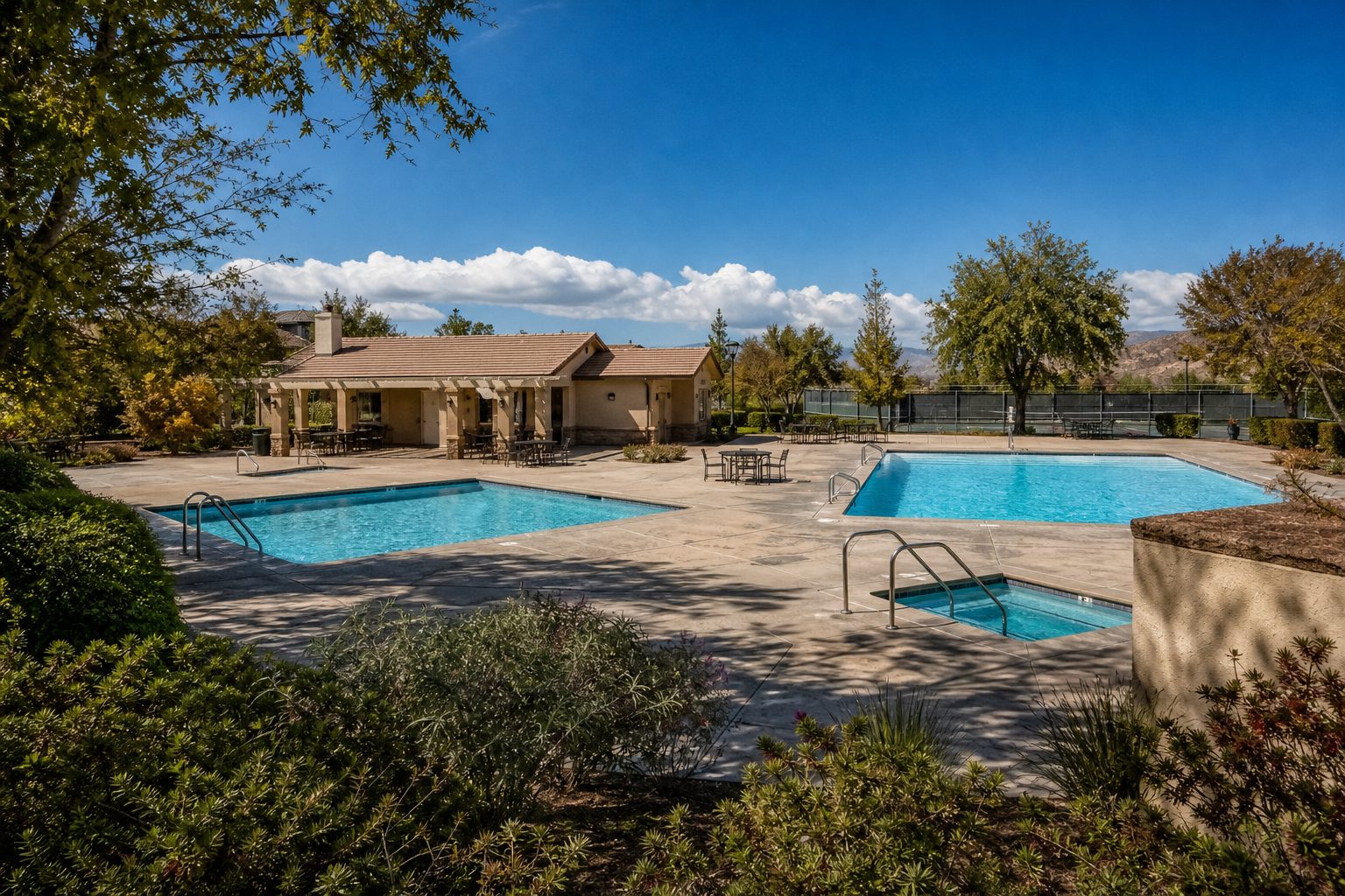 Resort-style pool amenities framed by desert landscaping at North Park Valencia community with clubhouse and tennis facilities.